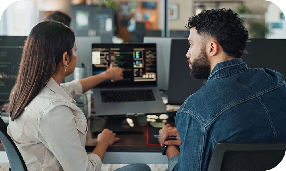 Two colleagues review critical data while one points at result displayed on a laptop with the other looking on intently. 