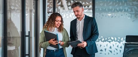 Two professionals smile and look at a tablet one of them is holding.