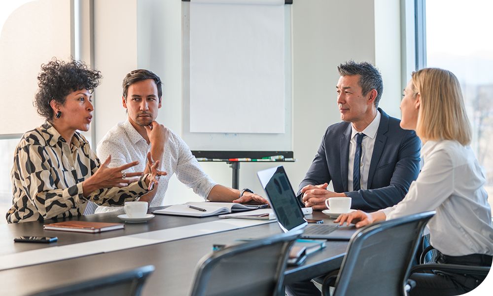 Four colleagues chat in a conference room.