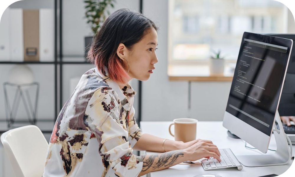 An individual types on a computer at their desk while looking at a monitor.