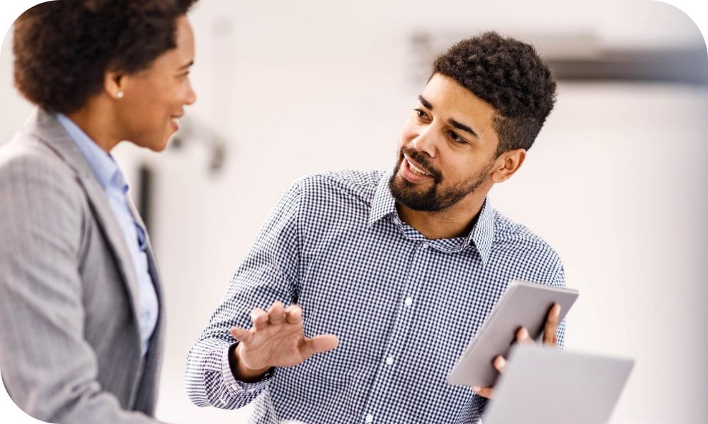Two professionals chat, while one gestures and holds a tablet.