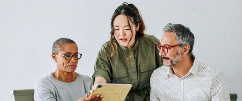 Three individuals look at a tablet together and discuss.