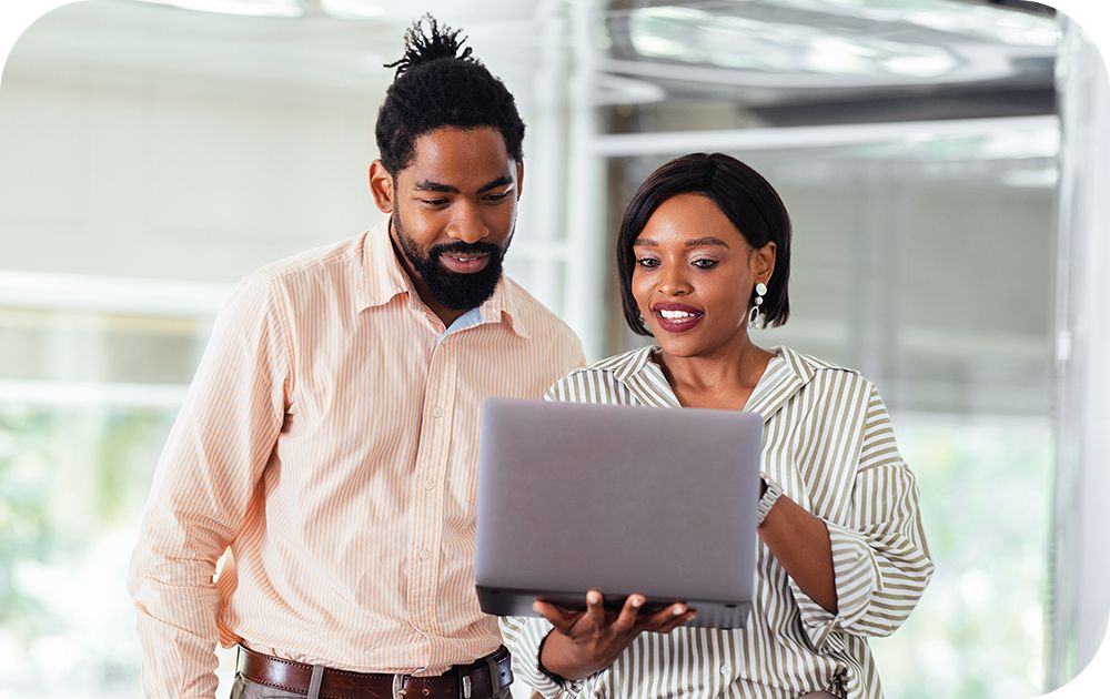 Two people stand next to each other while looking at a laptop one of them is holding.