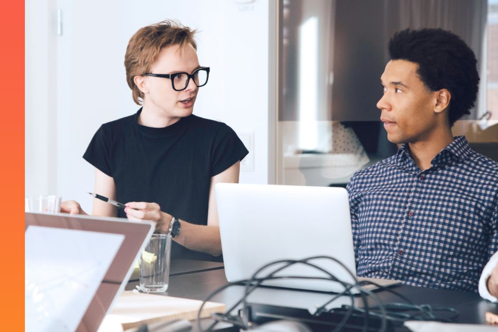 Two colleagues discussing issues passionately with laptops open on conference table. 