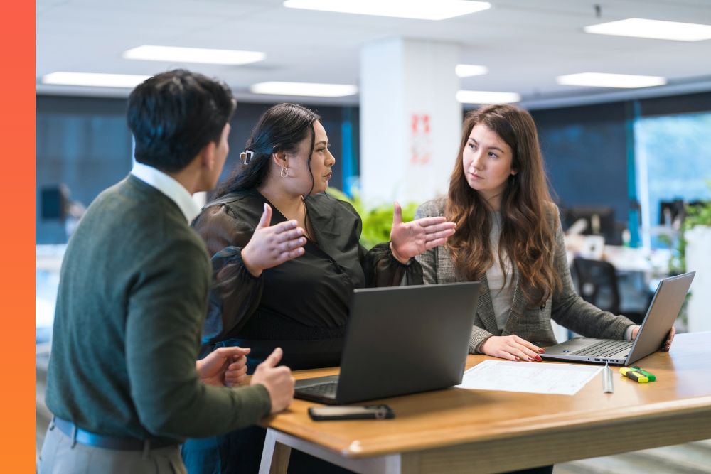  Three business people have a conversation with laptops in front of them