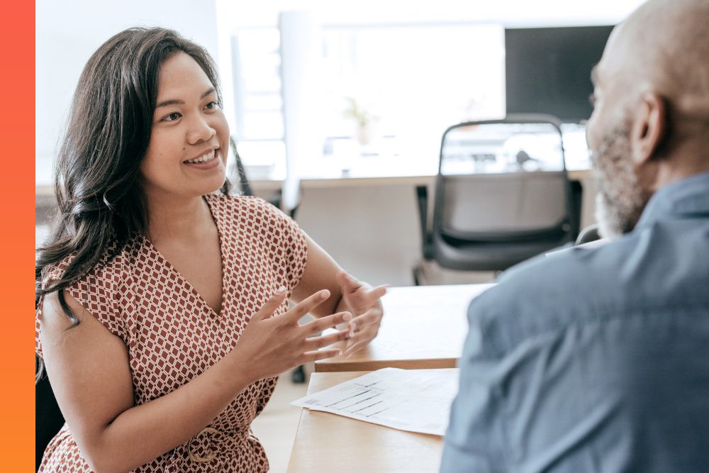 Two colleagues sitting at conference table in office building have a constructive discussion.