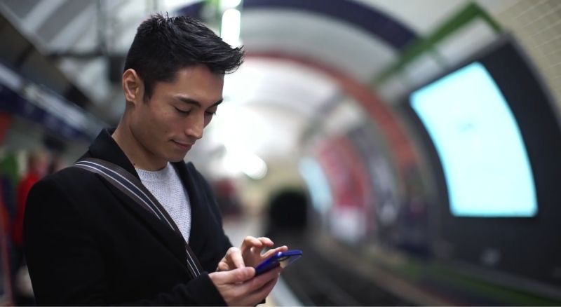 Mann schaut auf sein Telefon, während er auf einem Bahnsteig steht