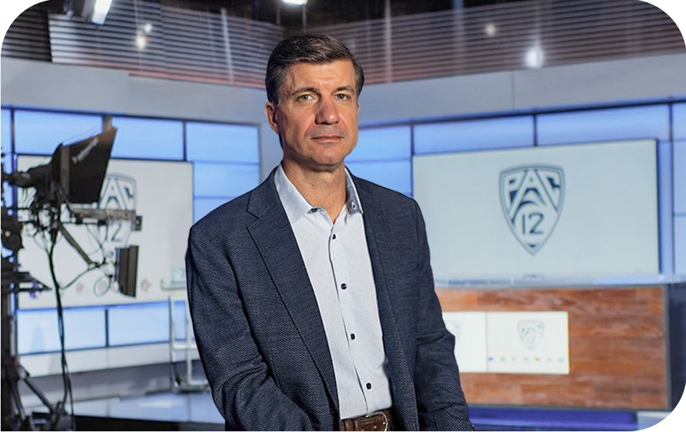 Michael Molinari, Senior Vice President of PAC‑12 Enterprises, in a TV studio with the Pac-12 logo visible in the background. 