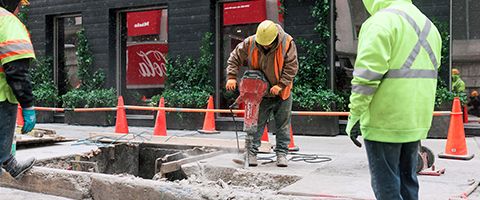 Lumen workers in hardhats and safety vests drill through concrete on Chicago sidewalk