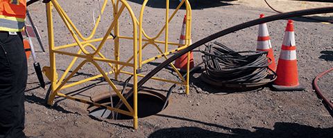 Two Lumen workers lower fiber into a manhole near the roadway