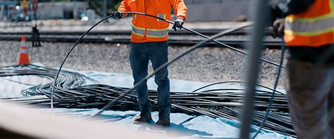 Two Lumen workers in orange safety vests shown from chest-down work together to lay out fiber cable