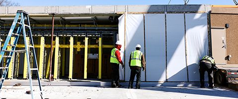 Three Lumen workers in white hardhats and yellow safety vests set up ILA shelter