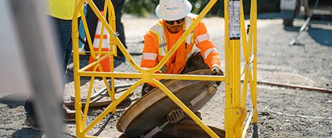 Two Lumen workers in hardhats and safety vests remove manhole cover to start fiber work