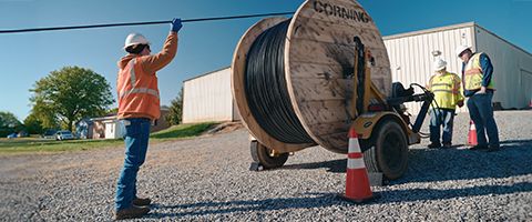 Three Lumen workers in hardhats and safety vests work with fiber roll