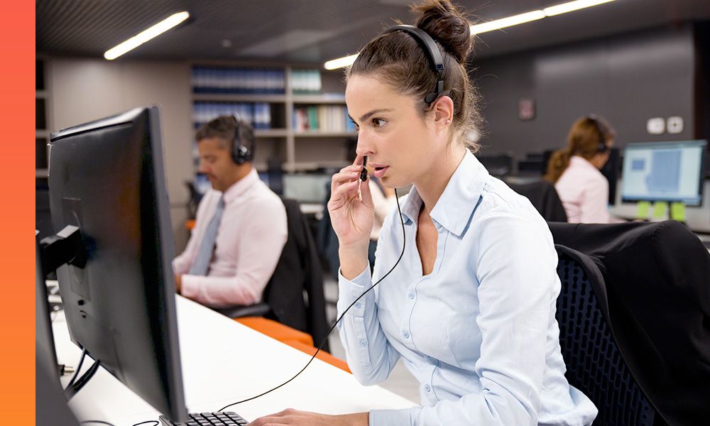 A person in a button-down shirt talks on a headset in a call center.