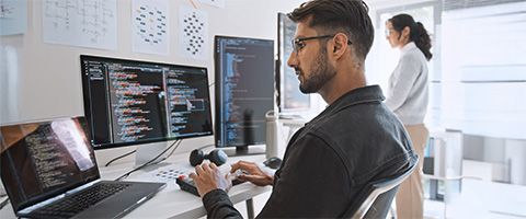 A person works on a computer at a table with several monitors.