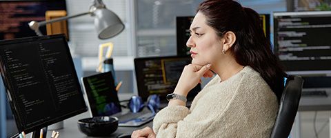 A person sits at a desk with several computers and concentrates.