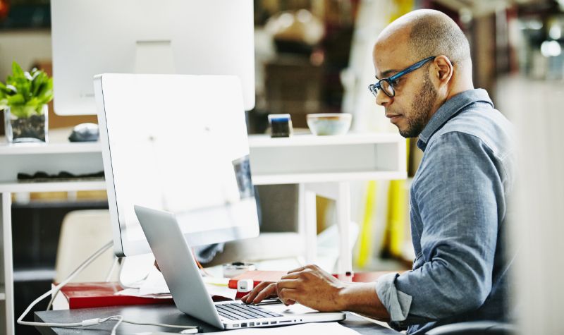 Erwachsener männlicher Technologieprofi, der an seinem Schreibtisch mit einem Laptop arbeitet