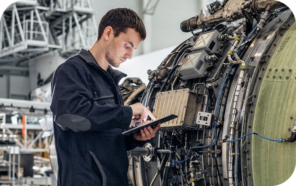 Person using a tablet to inspect engine components inside an industrial maintenance facility.