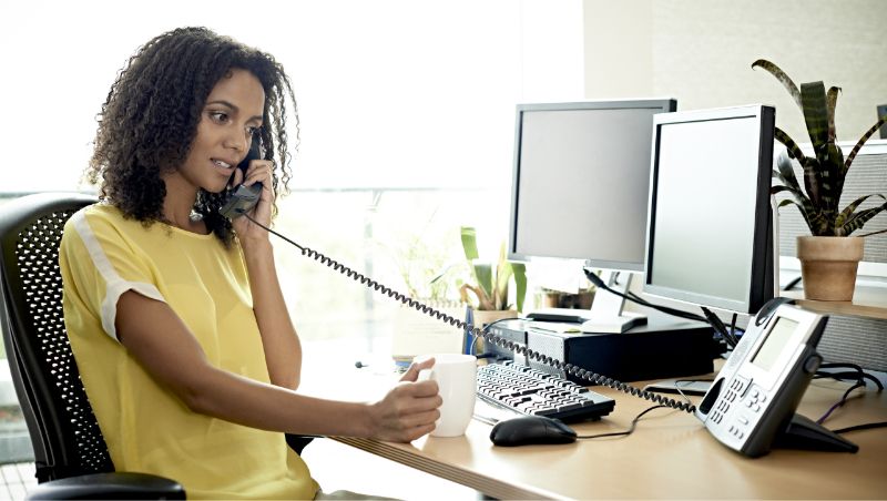 A person is shown in an office talking on a phone in front of a computer