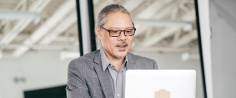 A person wearing glasses works on a laptop computer