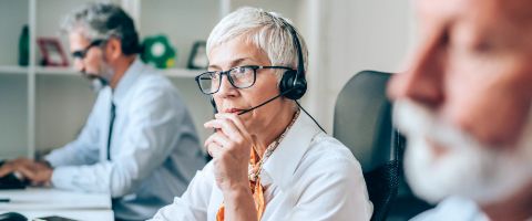 Person sitting at a row of computers with two other people while talking on a headset