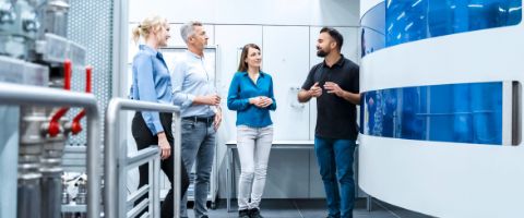 Four businesspeople standing together talking in a room full of servers and equipment 