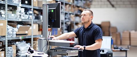 An individual works at a computer station in a warehouse.