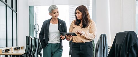Two businesspeople walk together while talking about something on a tablet screen.