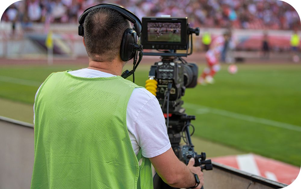 A cameraman in a green vest films a soccer field.