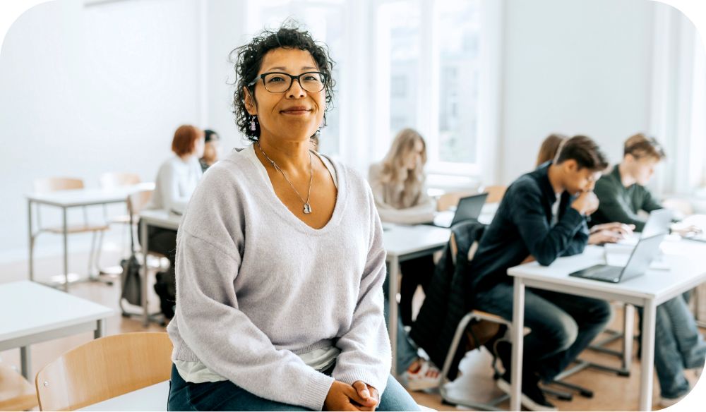 A teacher sits in a classroom while students work. 