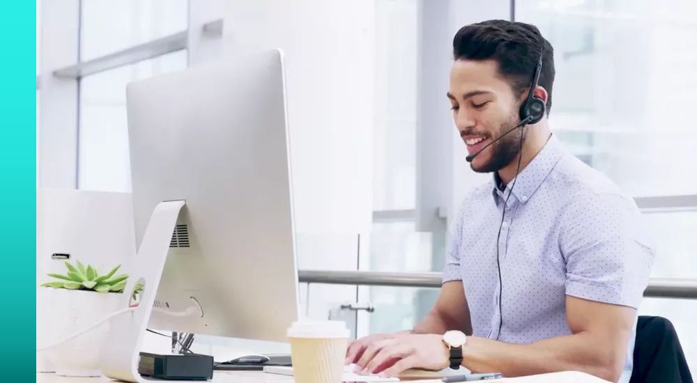 Person in collared shirt and headset talks while working at a desktop 