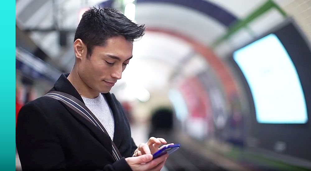 Person in a blazer stands in an underground transportation hub and sends a message using a telephone.