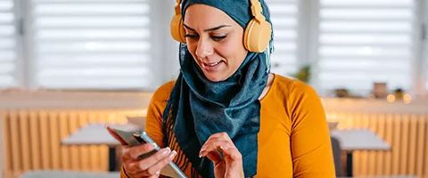 Person wearing headphones and looking down at a smart phone.