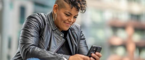 Person sitting and smiling down at a smart phone.