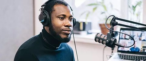 Person wearing headphones next to a microphone and a laptop showing a video conference call.