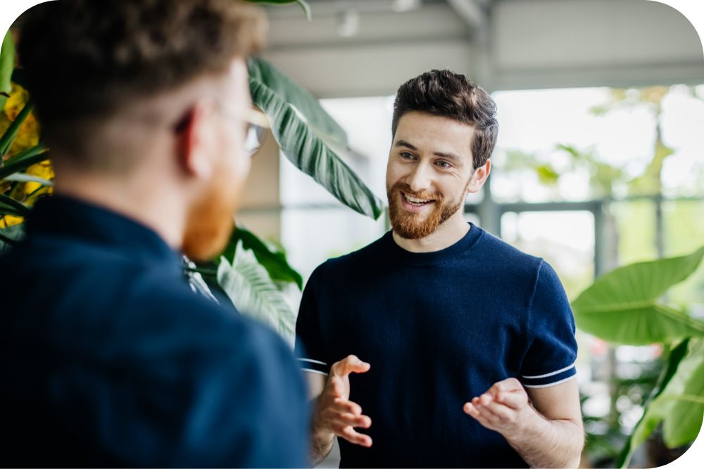 Two people have a conversation between two plants in a bright office space.