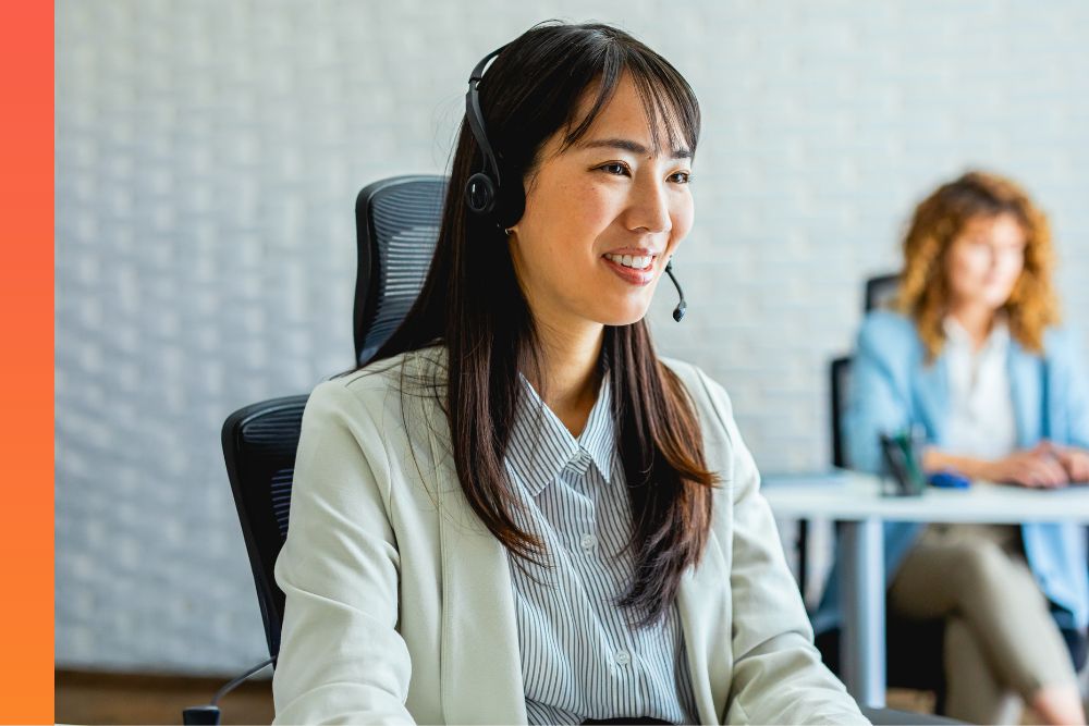 Businessperson sits in office chair with a headset on, smiling during a call. 