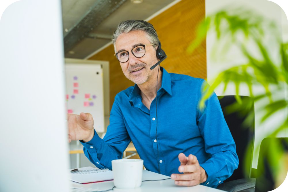 Businessperson at their desk in an office environment with a headset on, speaking on a call. 