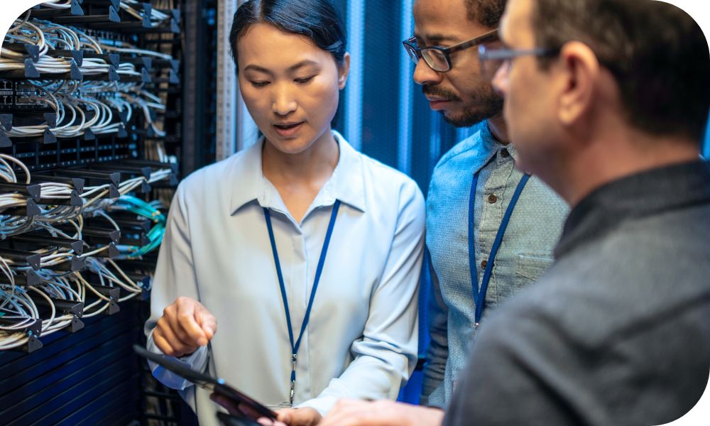 Three businesspeople standing next to a server and discussing something they see on one person’s tablet