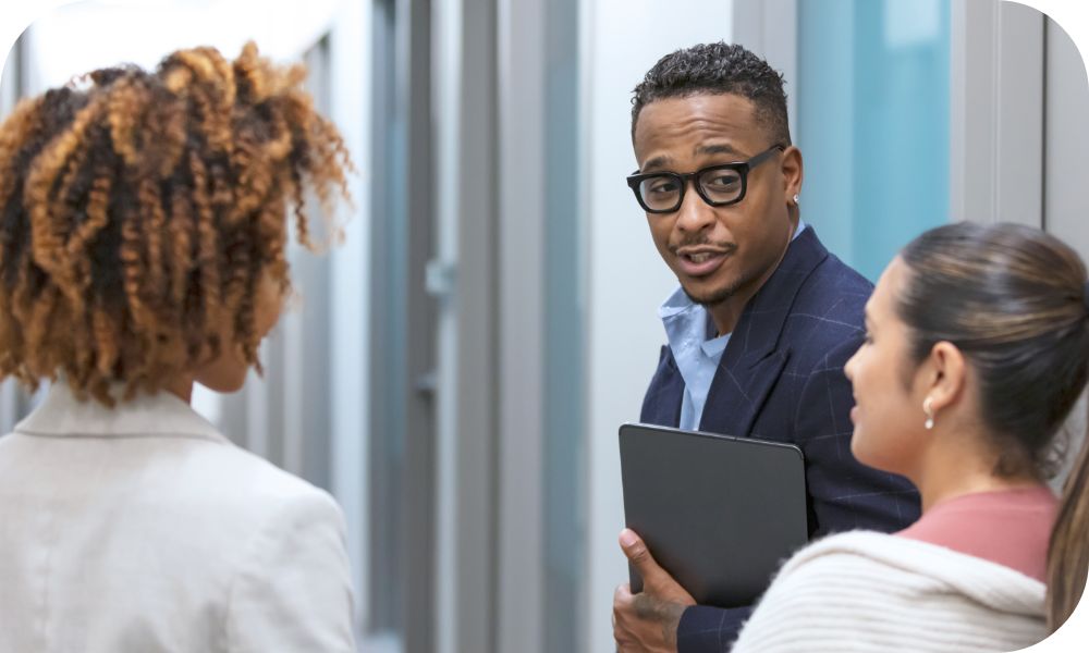 One security pro holding laptop talking to two other IT specialists as they walk down office corridor. 