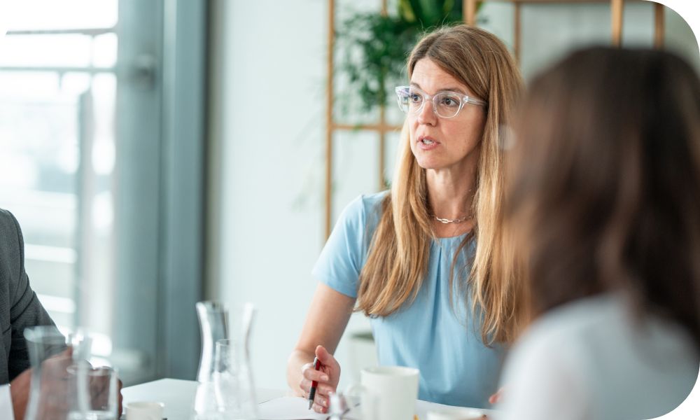 Three businesspeople talking and sitting around a conference table that has a jug of water on it