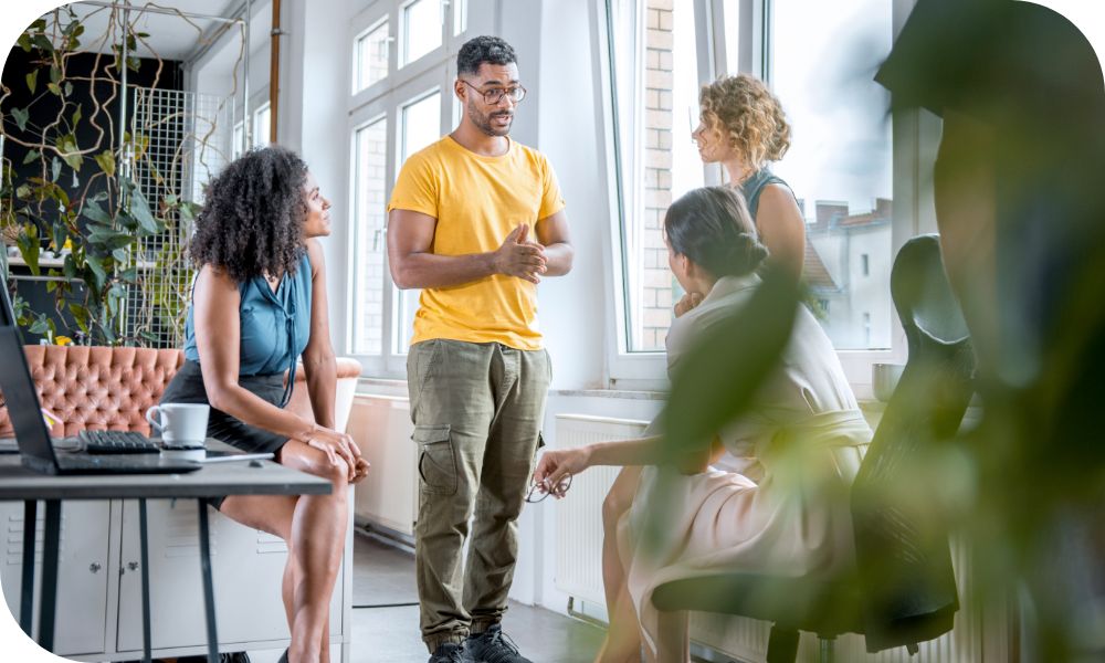 Four people gather near a window in a bright office to talk  