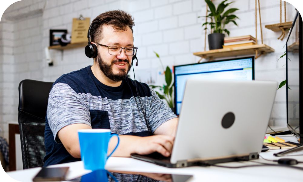 Person wearing a headset and working on a laptop in their office