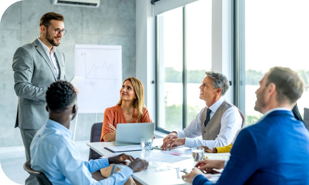 Businesspeople sitting at a conference table listening to a businessperson standing