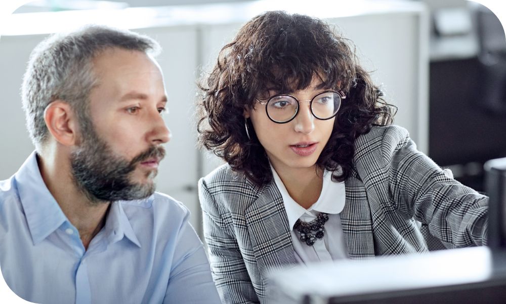 Two business professionals looking and point at computer monitor with serious intent