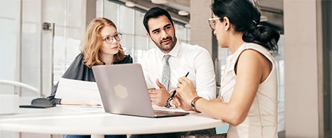 Three coworkers discuss something while looking at a laptop screen