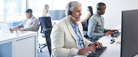 Five people with headsets sitting at computer desks in a contact centre.