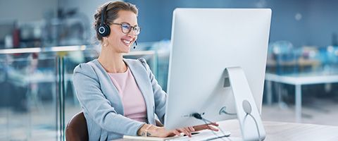  A woman wearing a headset works on a desktop computer and smiles 