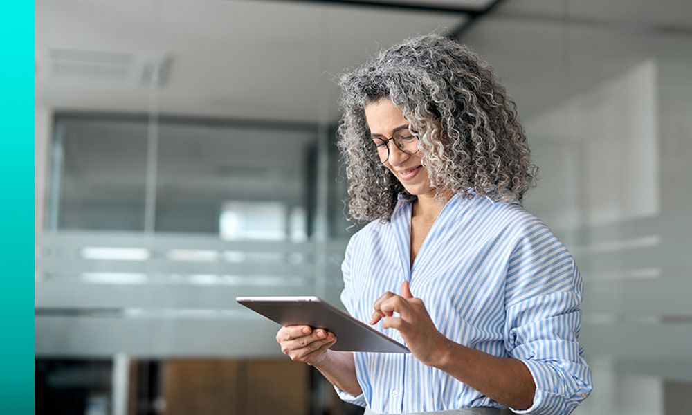 Person in a striped button-down shirt works on a tablet and smiles.